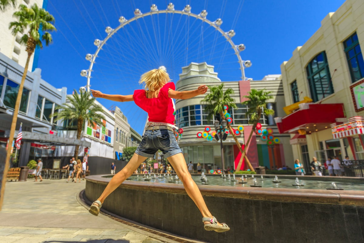 Blonde woman jumping at center of Las Vegas in a sunny day, blue sky. Ferris Wheel, the world