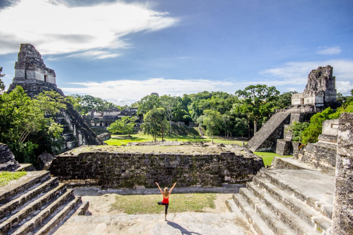 young female traveler doing morning yoga at tikal temples in guatemala